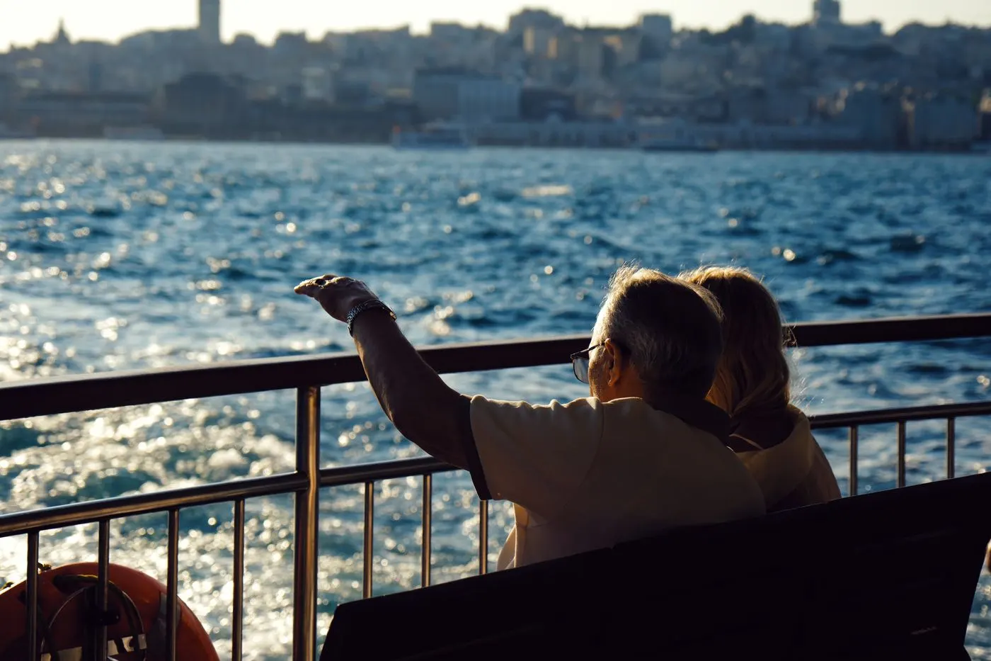 Casal sentado no deck de um barco observando a orla ao entardecer